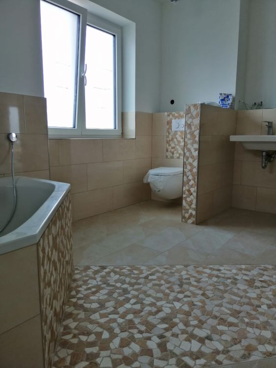 beigefarbenes Badezimmer mit Mosaikfliesen. Das Badezimmer hat eine große Badewanne und installierte Toilette