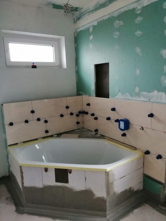 Das Badezimmer wird in Beige gefliest, bevor das Mosaik an der Badewannenwand angebracht wird.